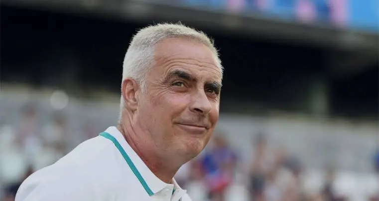 Smiling man with short gray hair in a white polo shirt at a sports stadium.