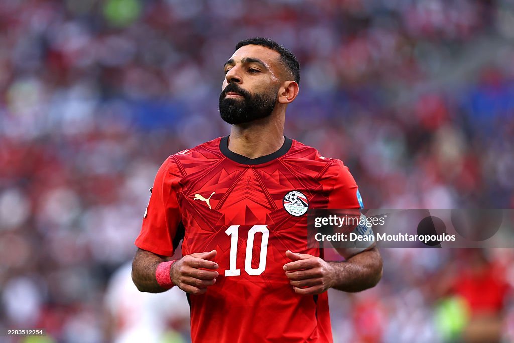Egyptian national football team player in a red jersey with number 10, jogging on the pitch during a match, crowd blurred in the background Egyptian national football team player in a red jersey with number 10, jogging on the pitch during a match, crowd blurred in the background