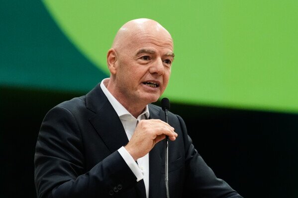 Bald man in a dark suit speaking into a microphone at a podium on a stage with a green backdrop. Bald man in a dark suit speaking into a microphone at a podium on a stage with a green backdrop.