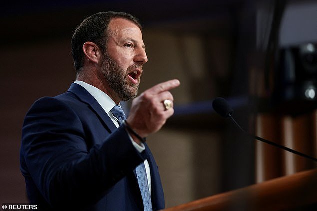 Man in a navy suit speaks at a podium, pointing his index finger as a microphone stands nearby.