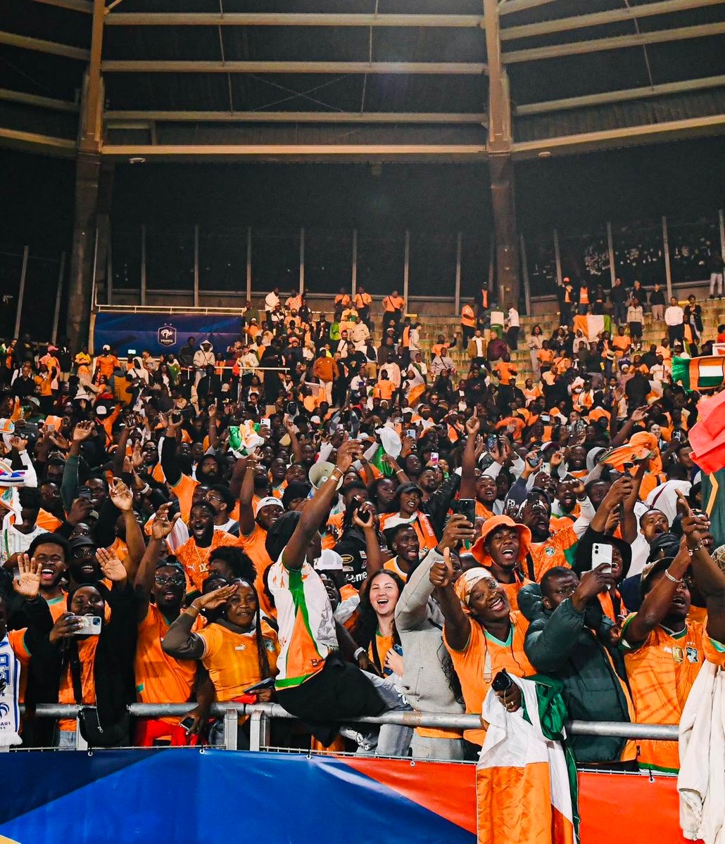 Large crowd of fans in an indoor arena, many wearing orange, cheering and taking photos.