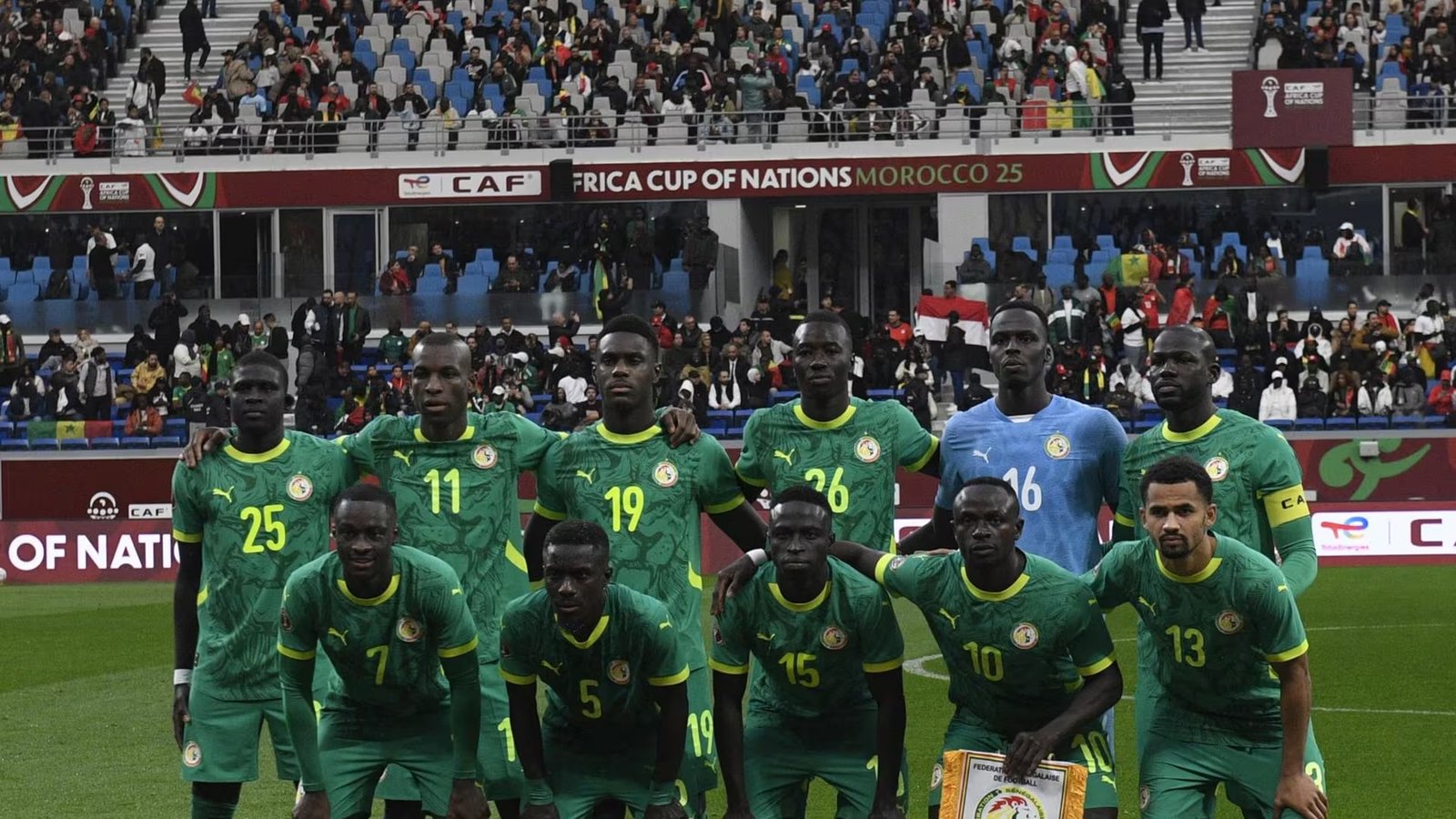 Senegal national football team posing for a pre-match photo on the pitch with fans in the stands.