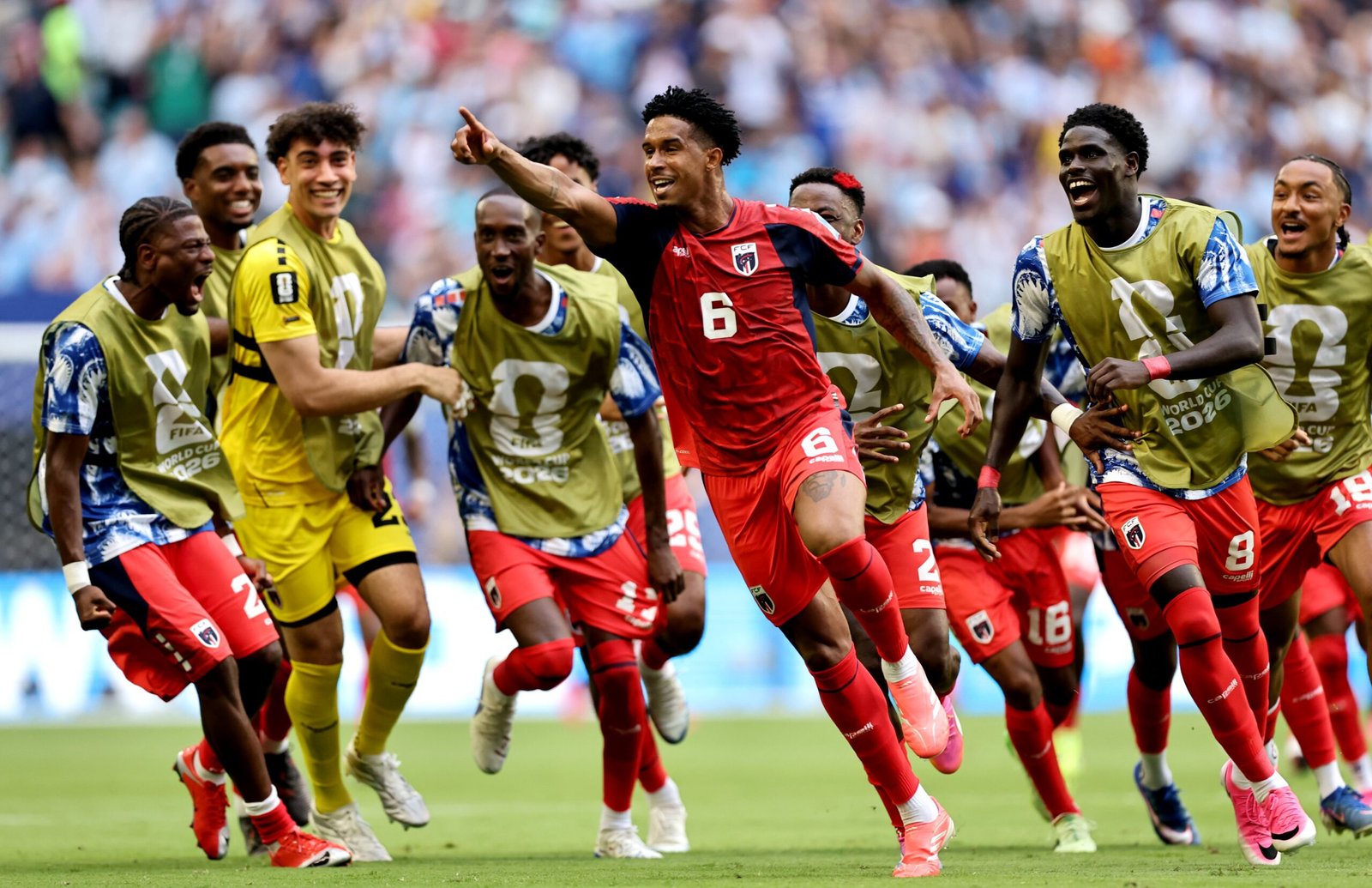 Group of soccer players in red and gold uniforms celebrate a goal on the pitch with a cheering crowd in the stands