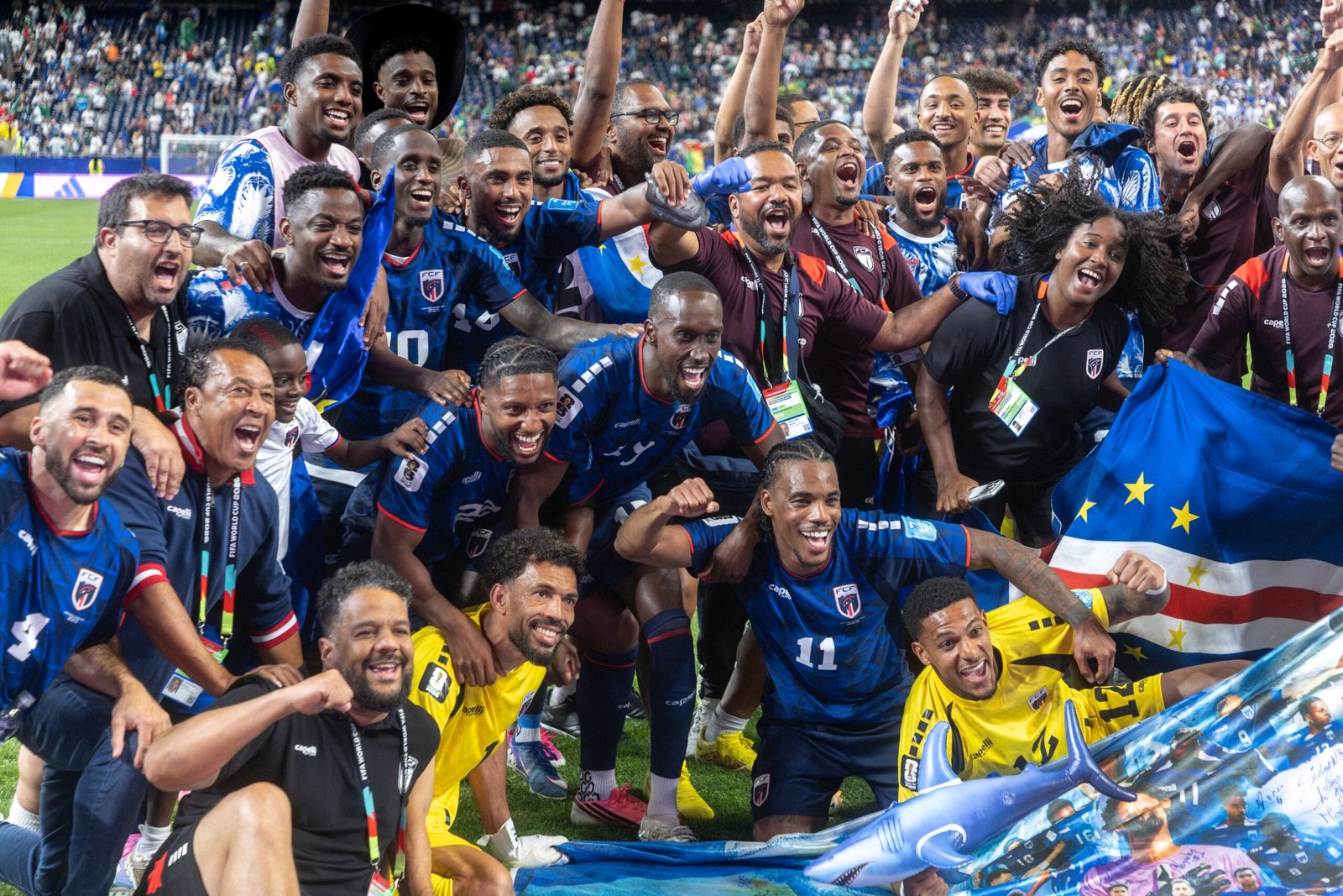 Group of soccer players celebrating together on the field with fans in the stands behind them Group of soccer players celebrating together on the field with fans in the stands behind them