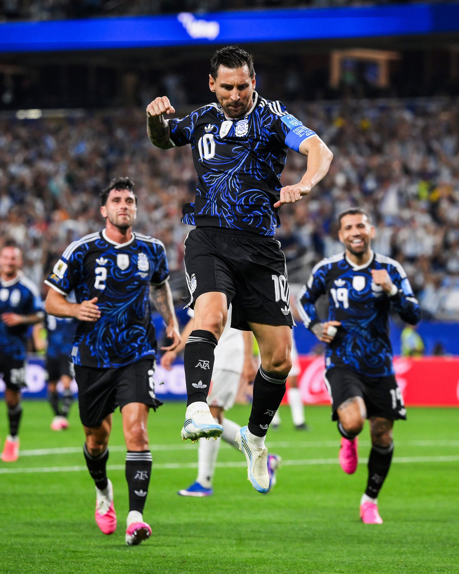 Central player wearing number 10 jumps in celebration on a soccer pitch, teammates behind him in blue-and-black kits, crowd in stadium Central player wearing number 10 jumps in celebration on a soccer pitch, teammates behind him in blue-and-black kits, crowd in stadium