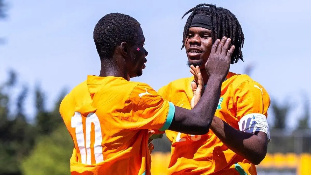 Two soccer players in orange jerseys celebrate with a high-five on a sunny field, one wearing number 10 on his back.