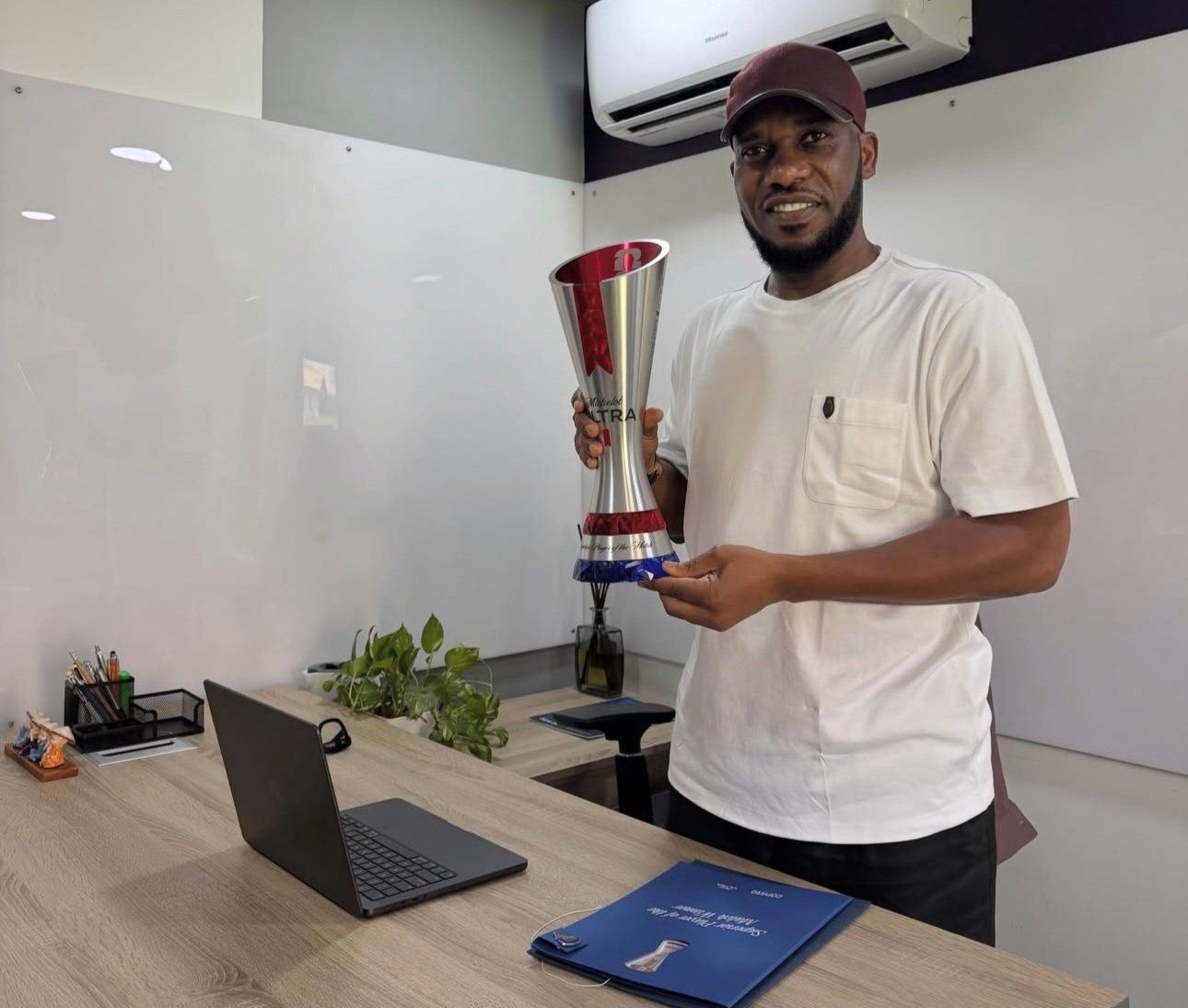 Man in a white shirt holds a tall silver trophy with red accents in an office setting.