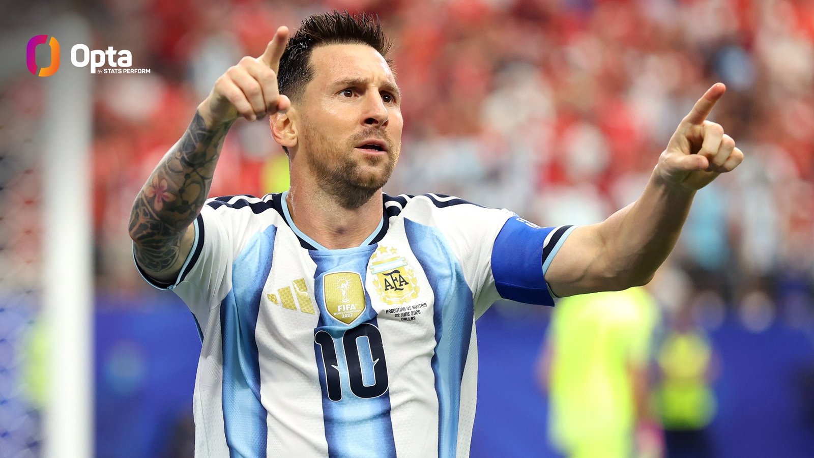 Argentine soccer player in a light-blue and white jersey celebrates with arms raised, pointing toward the crowd, stadium blurred behind him (Opta logo top-left).