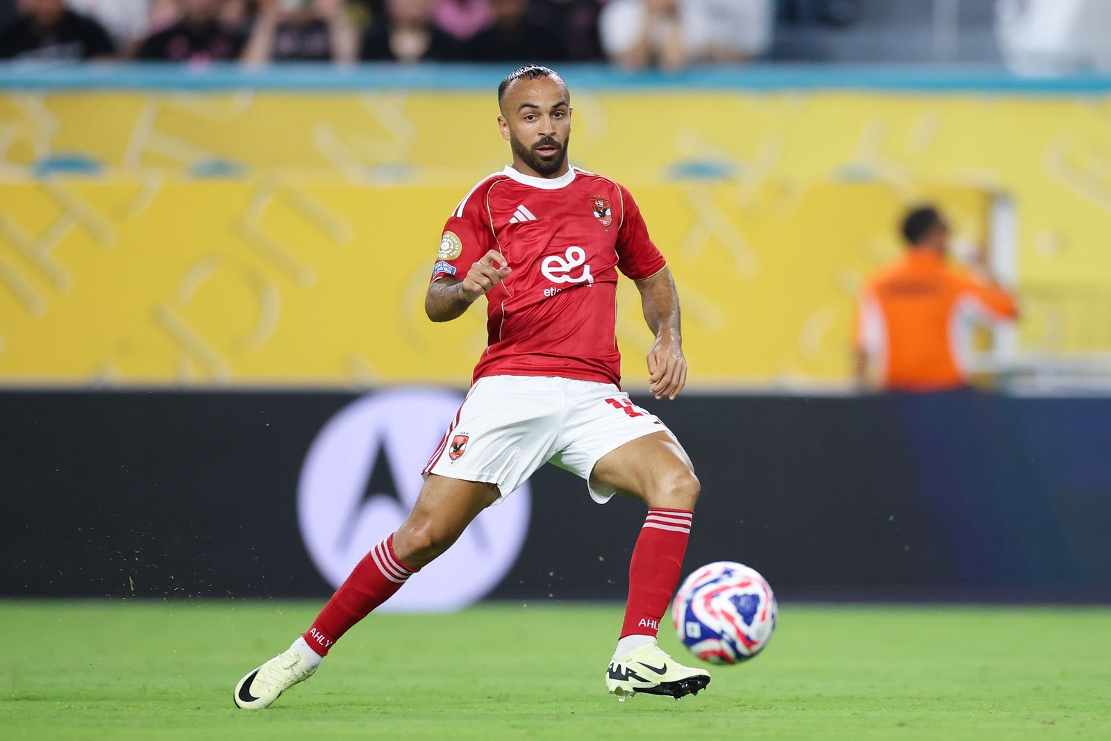 Soccer player in red jersey and white shorts sprinting after the ball on a green pitch in a match setting. (informative)