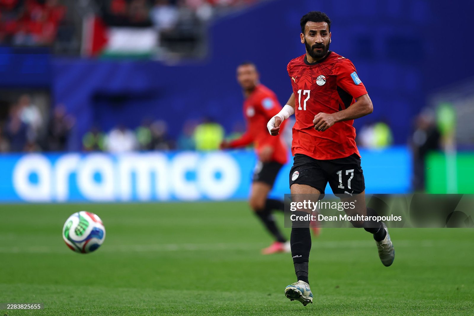 Soccer player in a red jersey with number 17 runs toward the ball on a green pitch during a match. Soccer player in a red jersey with number 17 runs toward the ball on a green pitch during a match.