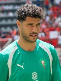 Male soccer player in a green training jersey with a Puma logo, on a stadium pitch with blurred fans in the background. Male soccer player in a green training jersey with a Puma logo, on a stadium pitch with blurred fans in the background.