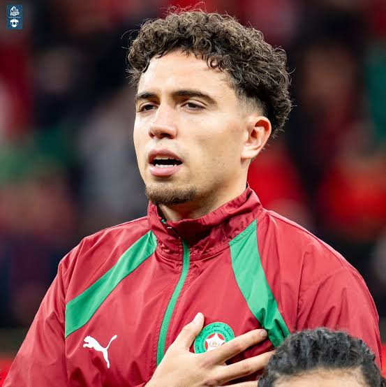 Male footballer in a red Portugal jacket with green accents, hand on his chest and looking ahead. Male footballer in a red Portugal jacket with green accents, hand on his chest and looking ahead.