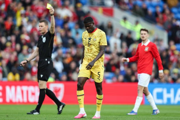 Soccer scene with a yellow-clad player wearing number 5 as the referee shows a yellow card nearby and teammates watch on the field far behind. Soccer scene with a yellow-clad player wearing number 5 as the referee shows a yellow card nearby and teammates watch on the field far behind.