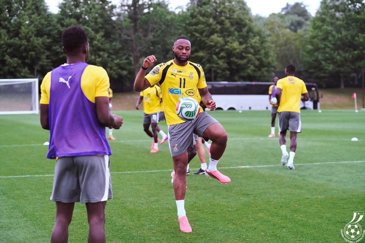 Soccer training drill: a player in a yellow jersey controls the ball while others watch on a green field with a bus in the background Soccer training drill: a player in a yellow jersey controls the ball while others watch on a green field with a bus in the background