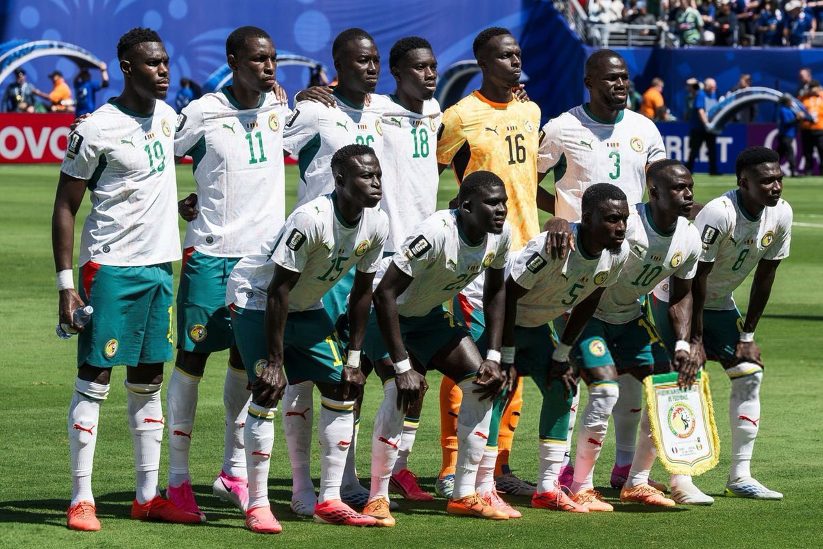 Group of Senegal national football team players posing for a pre-match photo on the field in white jerseys and green shorts, goalkeeper in orange in back row