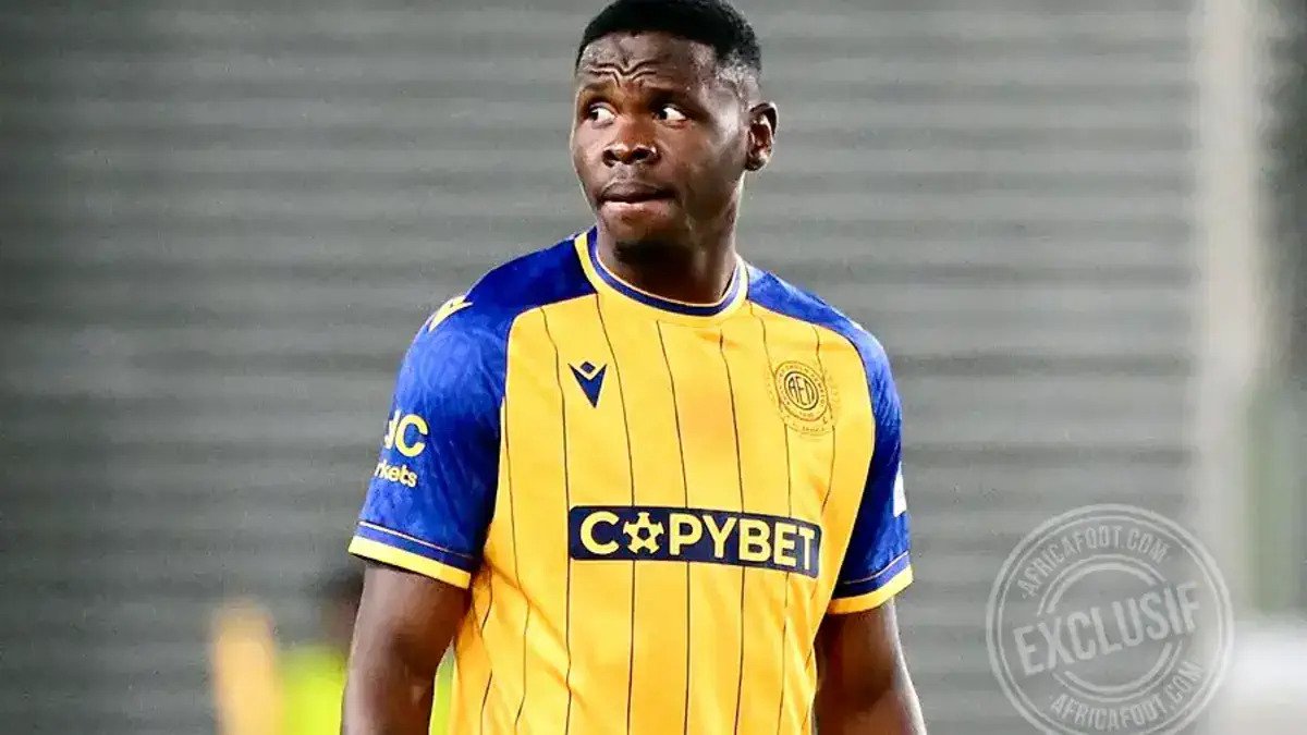 Footballer in a yellow and blue jersey with COPYBET sponsor looking to the left on a football pitch.