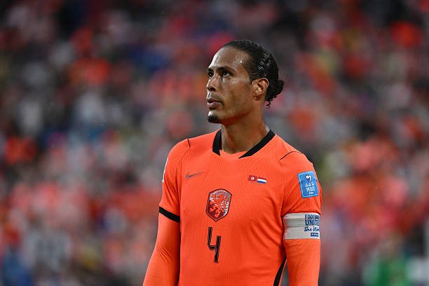 Dutch national team soccer player wearing an orange jersey with number 4 during a match, with a captain's armband visible. Dutch national team soccer player wearing an orange jersey with number 4 during a match, with a captain's armband visible.