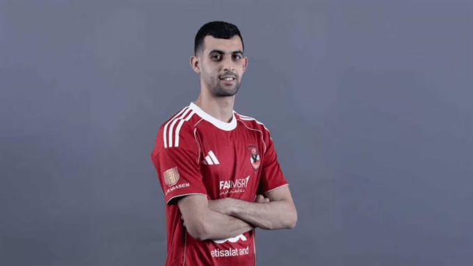 Man wearing a red football jersey with arms crossed, posing against a gray background.