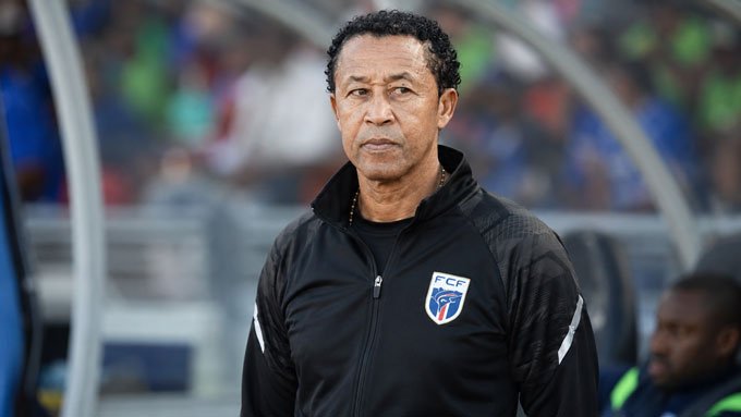 brito – African Football Male soccer coach standing on the sideline in a black jacket with a crest, focused gaze ahead. Male soccer coach standing on the sideline in a black jacket with a crest, focused gaze ahead.