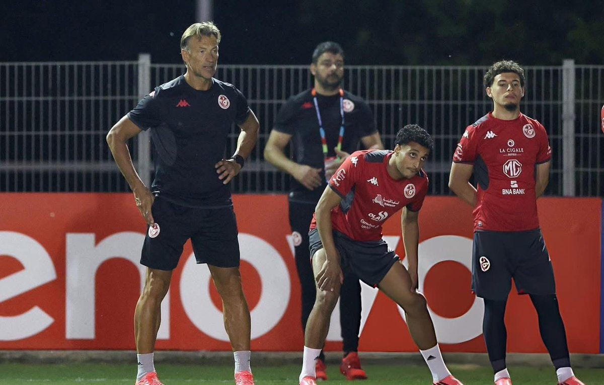 Coach and three players in red training kits standing on a field at night, listening to instructions.