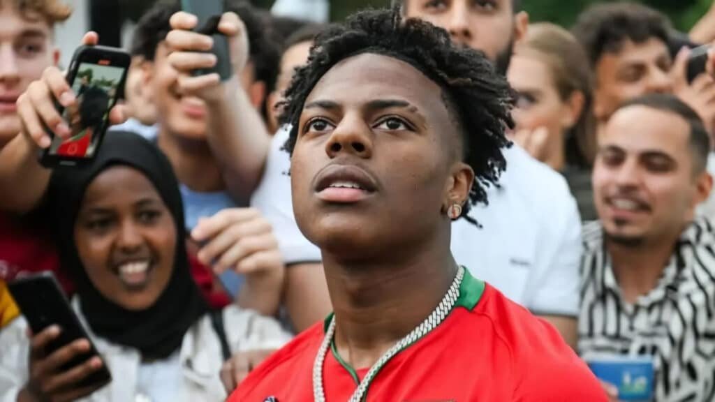 Young man in a red shirt looks up as a crowd and photographers surround him, taking selfies and pictures.