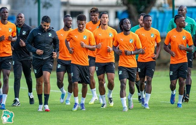 Soccer players in orange training kits jogging together on a green practice field. Soccer players in orange training kits jogging together on a green practice field.