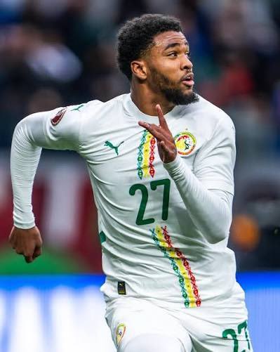 Senegal national team player in white kit with number 27, sprinting on a football field during a match. Senegal national team player in white kit with number 27, sprinting on a football field during a match.