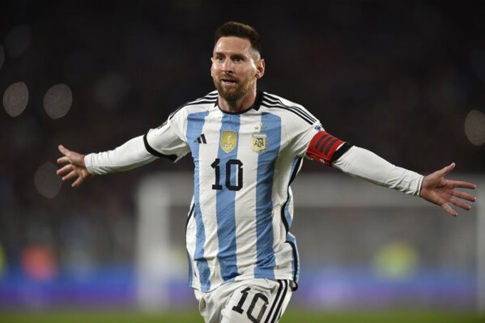 Argentine soccer captain wearing a light-blue and white striped jersey with number 10, arms outstretched in celebration on the pitch.