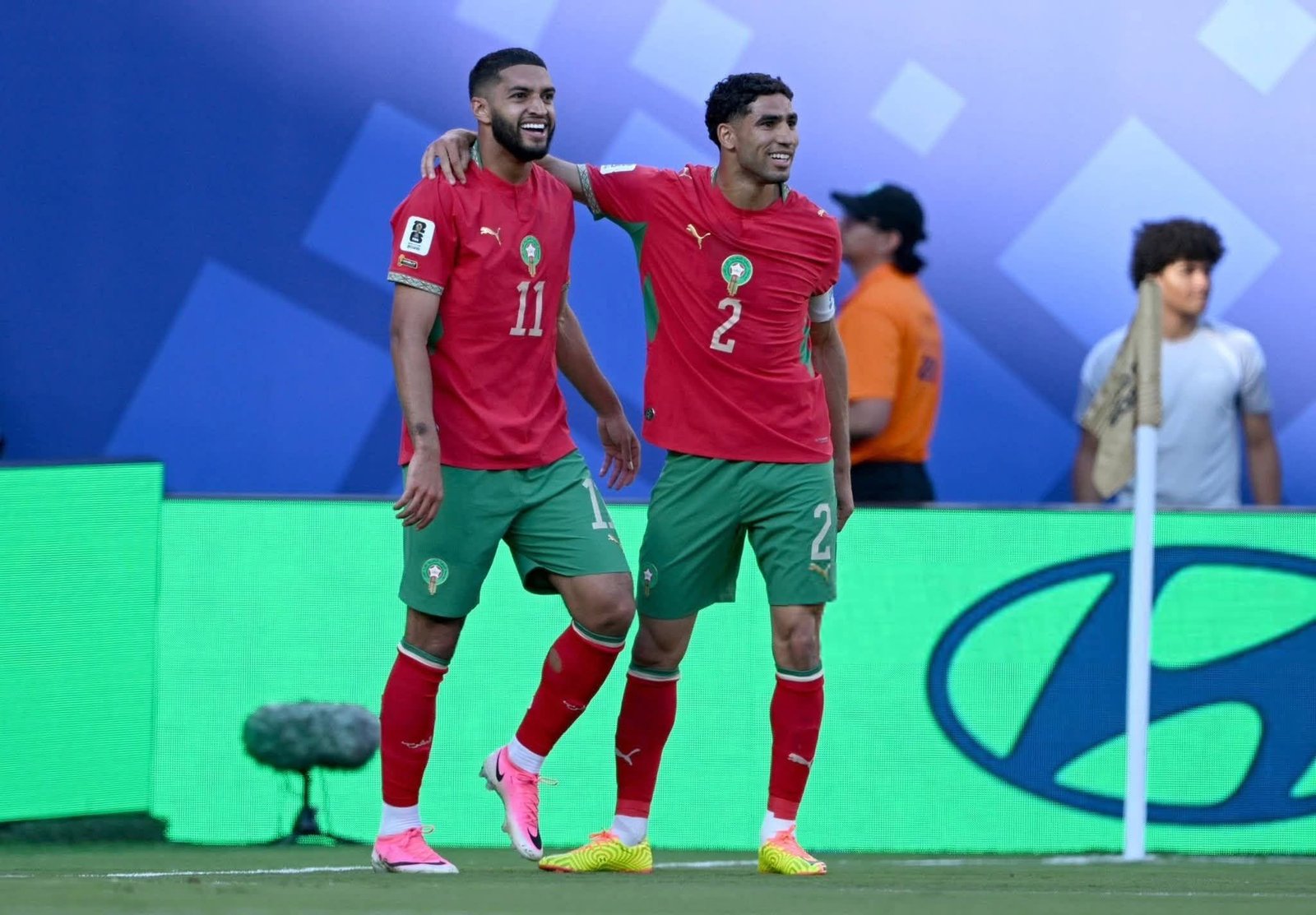 Two soccer players in red jerseys celebrate together with their arms around each other on a green field.