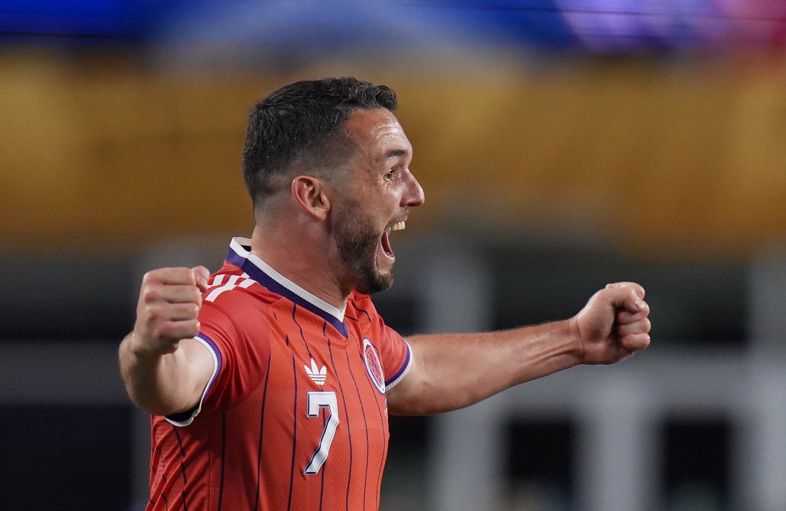 Soccer player in a red jersey with number 7 celebrates with fists raised in front of a blurred crowd background. Soccer player in a red jersey with number 7 celebrates with fists raised in front of a blurred crowd background.