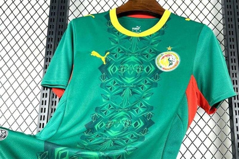 Green soccer jersey with yellow collar and geometric pattern, Puma logo on the chest, circular team crest on the opposite chest, red underarm panels, hanging on a wooden hanger.