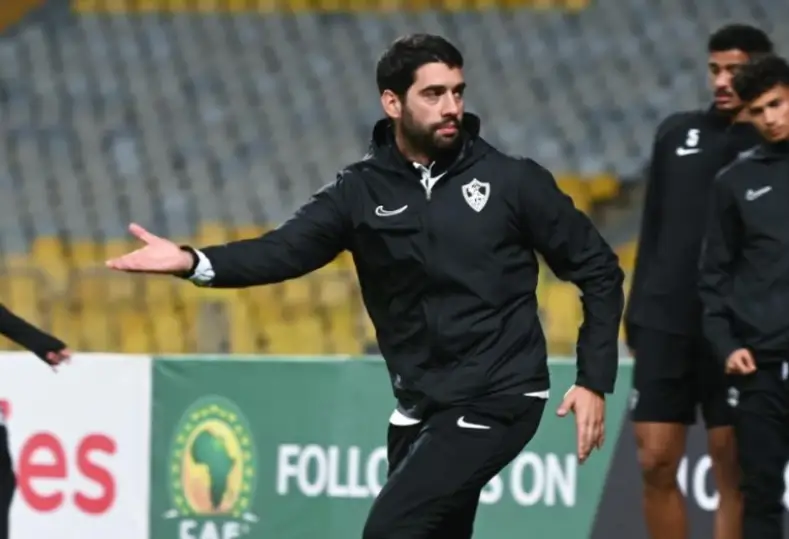 Male soccer coach in black tracksuit gesturing with an outstretched arm on a training field. Male soccer coach in black tracksuit gesturing with an outstretched arm on a training field.