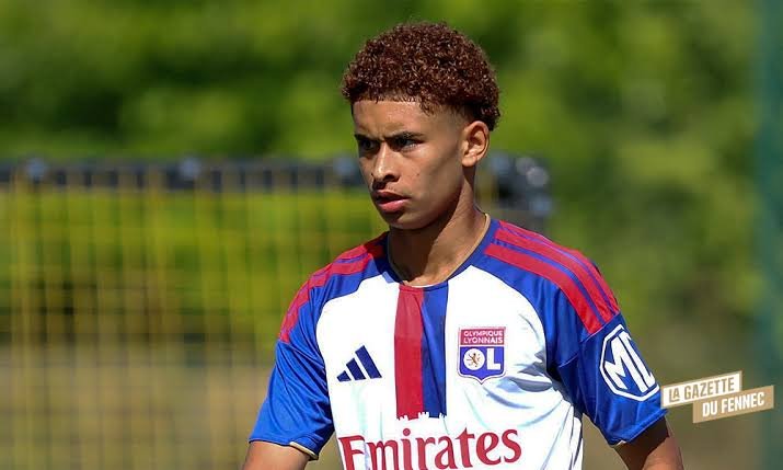 Young footballer in Olympique Lyonnais training kit on a practice field, focused and ready to play, with Emirates sponsor logo visible on the chest. Young footballer in Olympique Lyonnais training kit on a practice field, focused and ready to play, with Emirates sponsor logo visible on the chest.