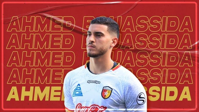 Portrait of a male soccer player in a white kit with a crest, standing against a red background with the name AHMED repeated. Coca‑Cola sponsor visible on jersey. Portrait of a male soccer player in a white kit with a crest, standing against a red background with the name AHMED repeated. Coca‑Cola sponsor visible on jersey.
