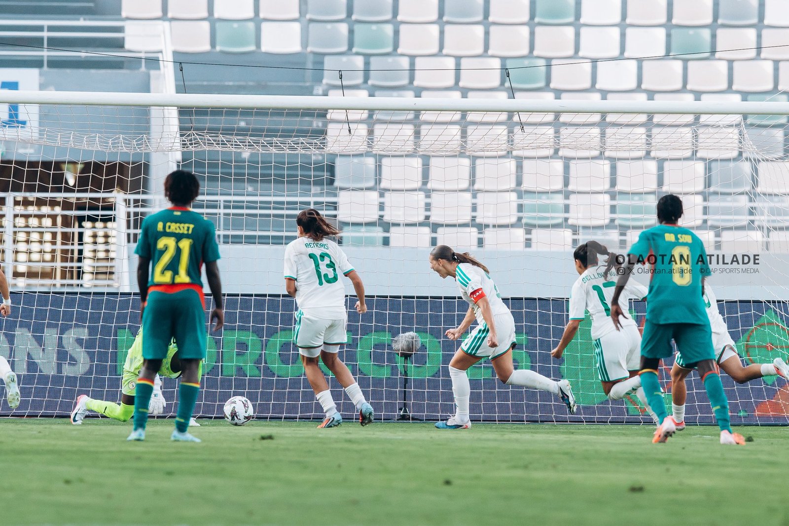 Soccer players near the goal during a match, white and teal uniforms, ball by the net as players contest for a shot Soccer players near the goal during a match, white and teal uniforms, ball by the net as players contest for a shot