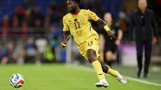 Soccer player in a yellow kit with number 13 chasing a ball on a grassy pitch during a match.