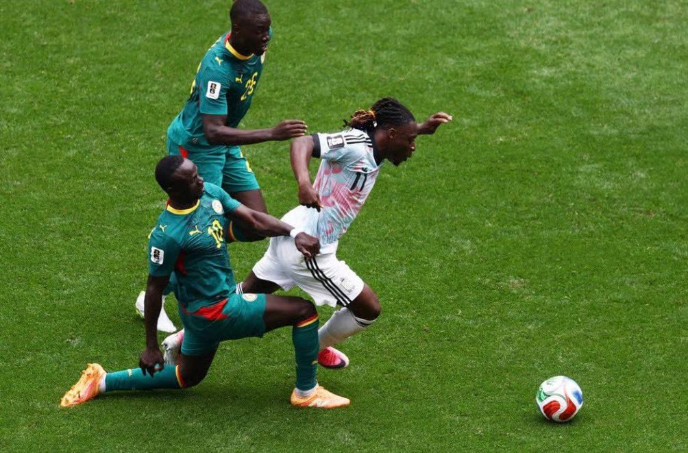 Soccer scene with three players challenging for a ball on a green field, one in white attempting to reach it. Soccer scene with three players challenging for a ball on a green field, one in white attempting to reach it.