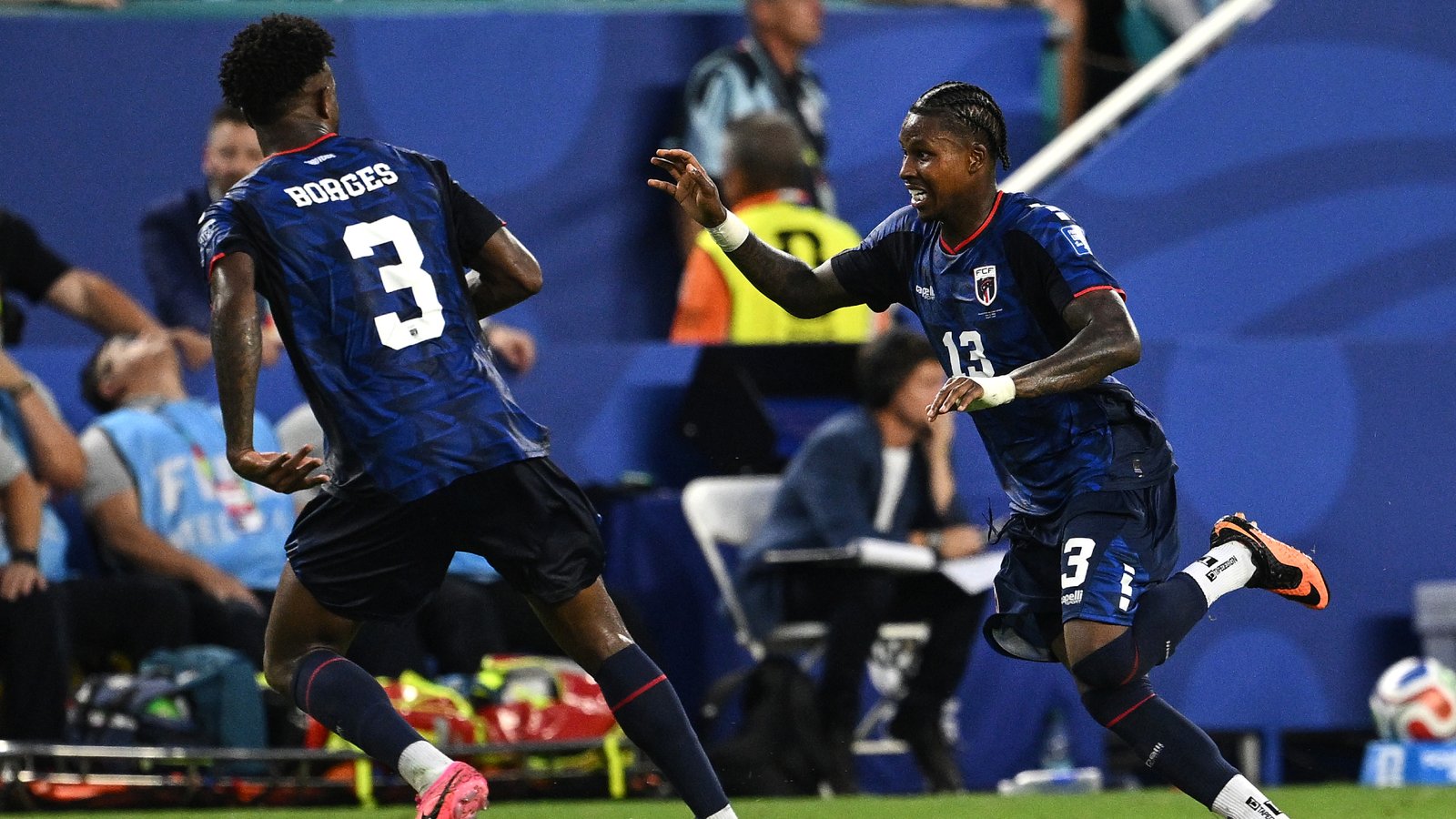 Two soccer players in blue uniforms sprint toward each other on the pitch, one with number 3 (Borges) on his back, celebrating a play from the side of the field. Two soccer players in blue uniforms sprint toward each other on the pitch, one with number 3 (Borges) on his back, celebrating a play from the side of the field.