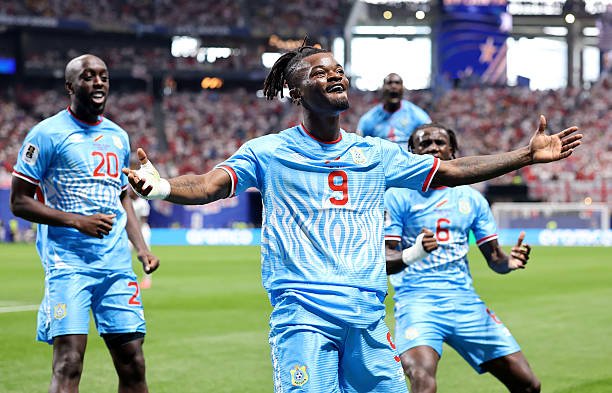 Nigerian soccer players celebrate a goal on the field, centered on the player wearing jersey number 9 with arms spread, teammates nearby, stadium full of fans. Nigerian soccer players celebrate a goal on the field, centered on the player wearing jersey number 9 with arms spread, teammates nearby, stadium full of fans.