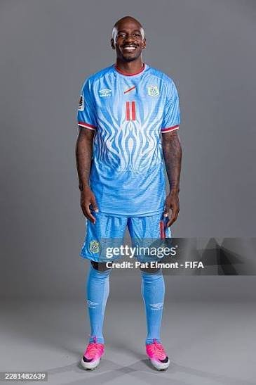 Tall dark-skinned footballer in a light blue jersey with number 11, blue shorts and socks, pink shoes, standing and smiling. Tall dark-skinned footballer in a light blue jersey with number 11, blue shorts and socks, pink shoes, standing and smiling.