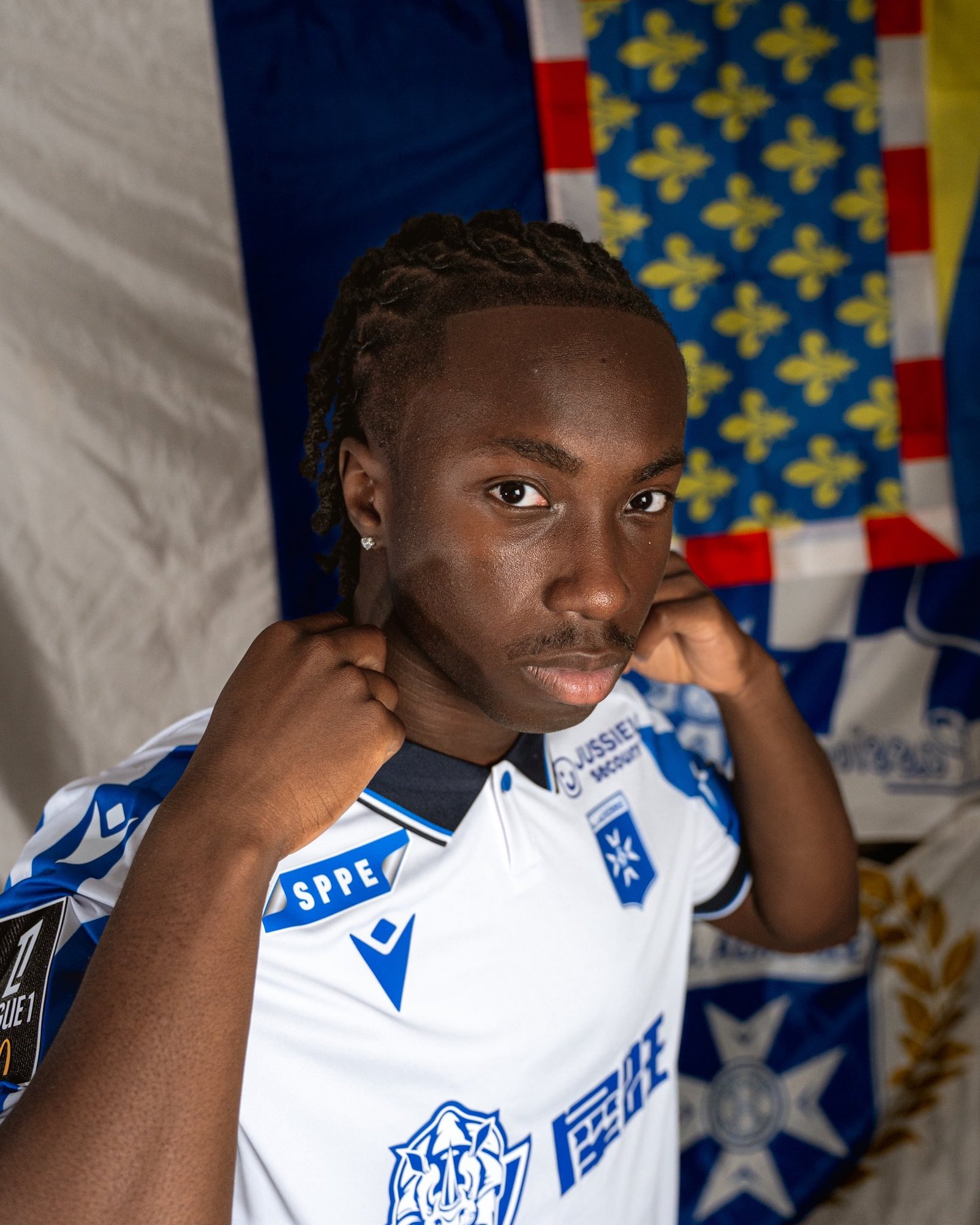 Portrait of a young cyclist in a blue-and-white racing jersey, adjusting his collar, with colorful banners in the background. Portrait of a young cyclist in a blue-and-white racing jersey, adjusting his collar, with colorful banners in the background.
