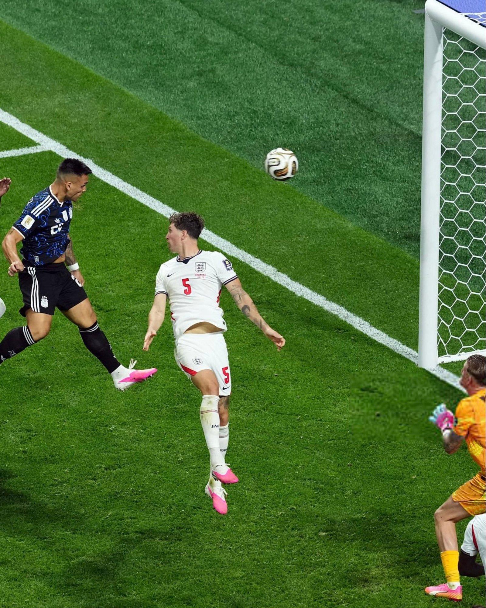 Soccer players near the goal as a ball sails toward the net, white England jersey number 5 in foreground. Soccer players near the goal as a ball sails toward the net, white England jersey number 5 in foreground.