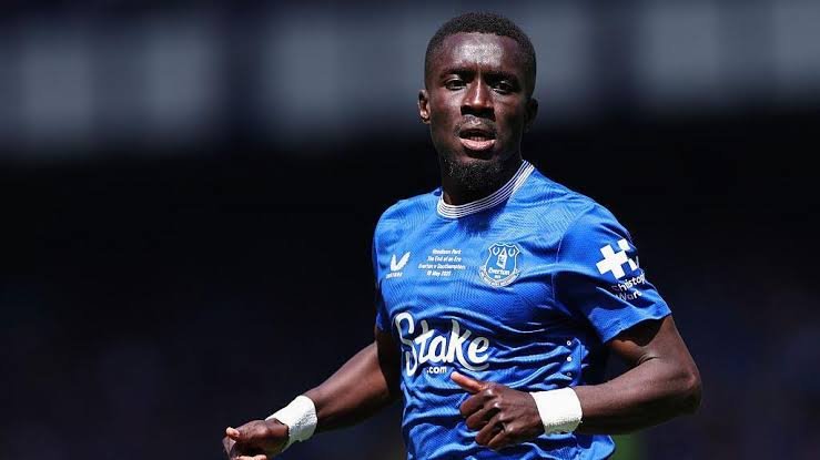 Male soccer player in a blue jersey with white wristbands running on a football pitch during a match.