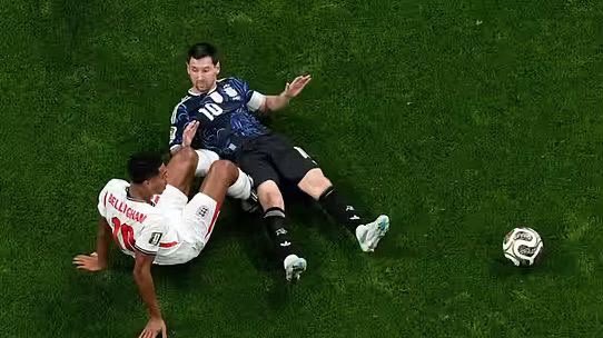 Two soccer players slide for the ball on a green pitch; one wears white with red number 10, the other in dark blue kit. Two soccer players slide for the ball on a green pitch; one wears white with red number 10, the other in dark blue kit.
