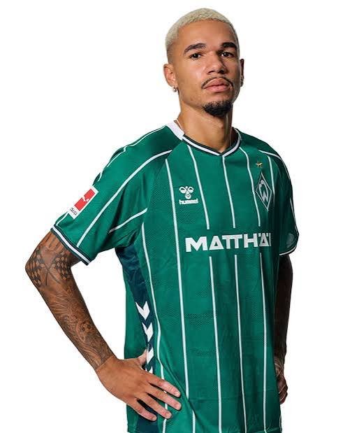Male model wearing a green Werder Bremen soccer jersey with white vertical stripes and sponsor text on the chest against a white background. Male model wearing a green Werder Bremen soccer jersey with white vertical stripes and sponsor text on the chest against a white background.