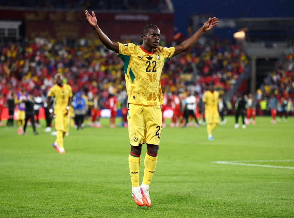 Soccer player in a yellow kit with number 22 raises arms on the green pitch during a match, with a crowd in the stands behind him. Soccer player in a yellow kit with number 22 raises arms on the green pitch during a match, with a crowd in the stands behind him. Soccer player in a yellow kit with number 22 raises arms on the green pitch during a match, with a crowd in the stands behind him. Soccer player in a yellow kit with number 22 raises arms on the green pitch during a match, with a crowd in the stands behind him.
