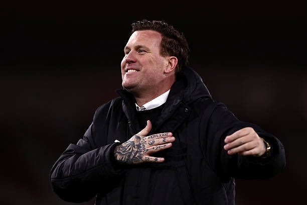 Smiling man with tattoos on his left hand wearing a black jacket, placing a hand over his chest in a gesture of gratitude or pride. Smiling man with tattoos on his left hand wearing a black jacket, placing a hand over his chest in a gesture of gratitude or pride.