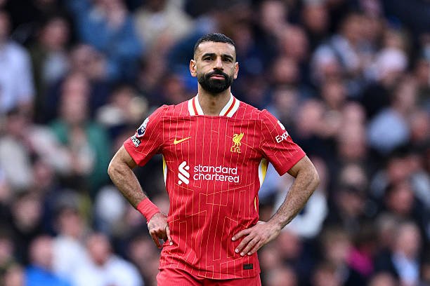 Mohamed Salah in Liverpool's red home kit standing on the pitch with hands on hips during a match Mohamed Salah in Liverpool's red home kit standing on the pitch with hands on hips during a match