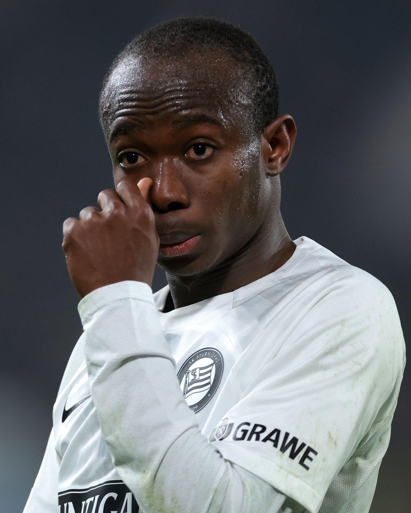 Close-up of a soccer player wiping sweat from his mouth, wearing a white jersey with a circular crest visible on the chest. Close-up of a soccer player wiping sweat from his mouth, wearing a white jersey with a circular crest visible on the chest.