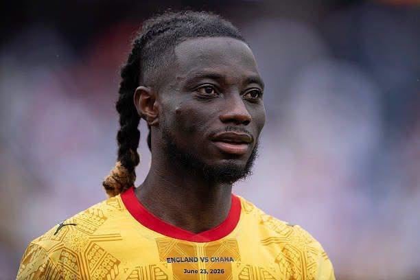 Close-up of a Black male footballer with a braided ponytail, wearing a yellow England vs Ghana jersey, looking ahead. Close-up of a Black male footballer with a braided ponytail, wearing a yellow England vs Ghana jersey, looking ahead.